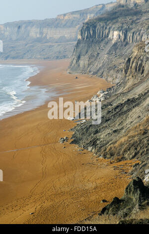 Une figure humaine solitaire marche sur une plage déserte de sable rouge falaises de falaise, ciel bleu clair, auto-isolation, distance sociale, Rocken End Isle of Wight Banque D'Images