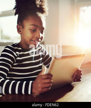 Close up Jolie Black Girl jouer à des jeux en ligne sur son ordinateur tablette avec des professionnels de l'expression du visage. Banque D'Images