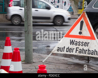 Vue détaillée d'une route mouillée intersection avec les voitures à Berlin avec cordons mis en place et l'inscription 'eau sur la route" Banque D'Images