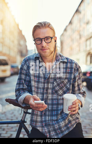 Portrait de jeune homme cool la vie dans la ville, tenant une tasse de café et son téléphone cellulaire Banque D'Images