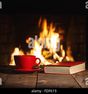 La tasse de café ou de thé et vieux livre sur table en bois près de cheminée. Vacances de Noël et d'hiver concept. Banque D'Images
