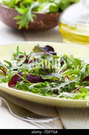 Mélange de feuilles de salade sur une assiette, de l'huile d'olive sur un fond de bois Banque D'Images