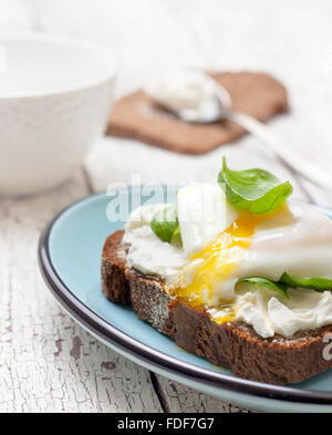 Toast avec oeuf poché, le fromage cottage et les feuilles de basilic sur un fond de bois Banque D'Images