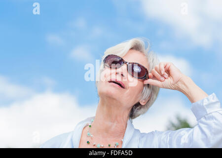 Ancien senior woman smiling with sunglasses en face de bleu ciel d'été Banque D'Images