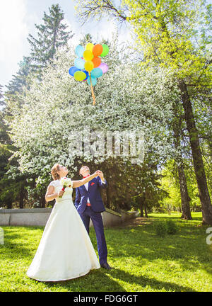 Heureux mariés à marcher ensemble dans un parc au printemps avec des ballons Banque D'Images