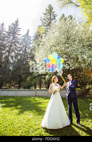 Heureux mariés à marcher ensemble dans un parc au printemps avec des ballons Banque D'Images