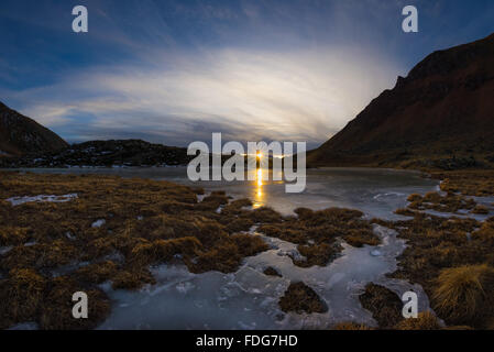 Lac alpin de haute altitude en terre idyllique. Reflet de la lumière du soleil sur la surface gelée. Sunstar rougeoyant à l'horizon à s Banque D'Images