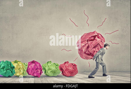 Businessman carrying avec grand effort boule de papier froissé comme signe de la créativité Banque D'Images