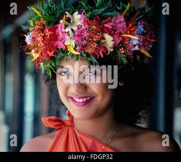 Une couronne florale tahitienne traditionnelle ajoute à la beauté de cette jeune fille souriante sur l'île de Moorea en Polynésie française dans l'océan Pacifique Sud. La guirlande de fleurs est appelée « hei » dans la langue tahitienne et est généralement portée par des épouses et des marié ainsi que par des danseuses dans des spectacles polynésiens pour les visiteurs des îles. Les coiffes multicolores sont faites avec une variété de fleurs fraîches, en particulier le tiare parfumé (gardenia) et le jasmin. Banque D'Images