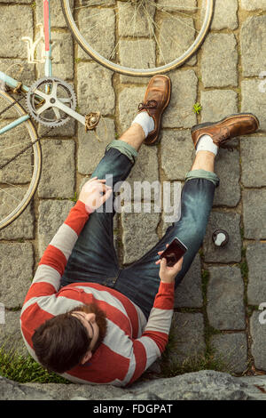 Jeune homme assis hipster et using cellphone Banque D'Images