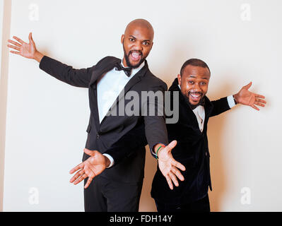 Deux hommes d'afro-américaine en costumes noirs qui posent des gestes, émotionnelle, souriant. Le port de liens à l'arc Banque D'Images