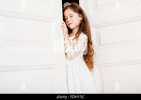 Peu jolie fille à la maison, de l'ouverture de la porte bien-habillé en robe blanche, adorable fée des dents de lait Banque D'Images