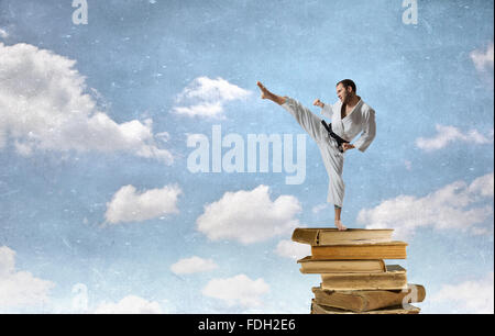 Jeune homme karaté déterminé on pile of books Banque D'Images