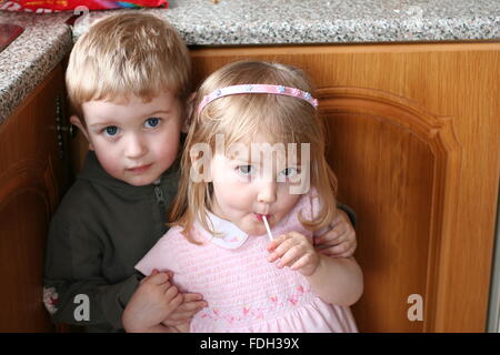 Cheveux blonds yeux bruns frère et sœur bénéficiant d''un lolly hugging, deux ans Banque D'Images