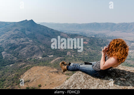 Fille à tête rouge assise sur le bord d'un rocher, prendre une photo du paysage dans le Mlilwane Wildlife Sanctuary au Swaziland Banque D'Images