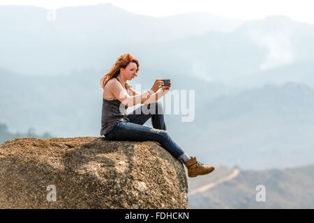 Fille à tête rouge assise sur le bord d'un rocher, prendre une photo du paysage dans le Mlilwane Wildlife Sanctuary au Swaziland Banque D'Images