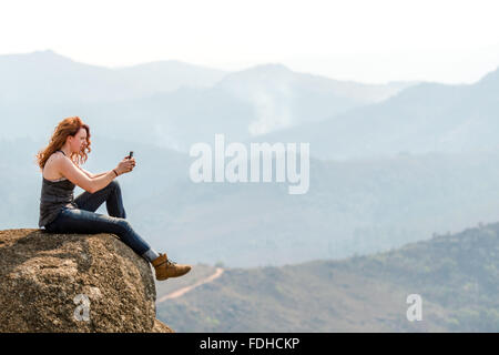 Fille à tête rouge assise sur le bord d'un rocher, prendre une photo du paysage dans le Mlilwane Wildlife Sanctuary au Swaziland Banque D'Images