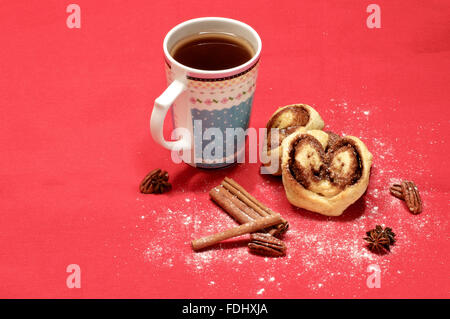 Petits pains cuits au four avec de la cannelle et du sucre avec une tasse de thé sur le tissu rouge Banque D'Images