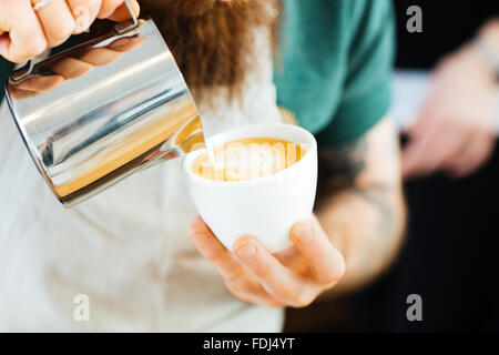 Closeup portrait of barista pouring lait en tasse de café au coffee shop Banque D'Images