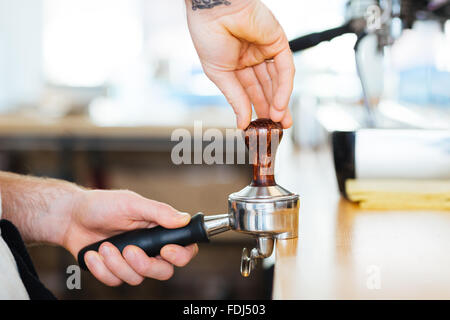 Gros plan du portafilter avec temper utilisé par les mains de café barista pour appuyer sur la Banque D'Images