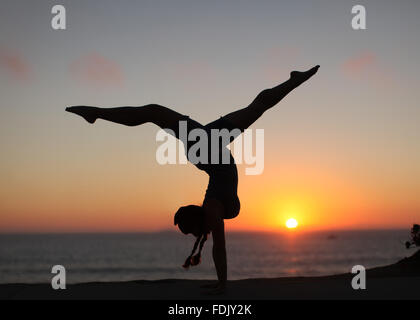 Silhouette d'une femme doing handstand avec les jambes sur la plage Banque D'Images