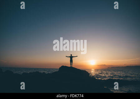 Silhouette d'un homme debout sur des rochers with arms outstretched Banque D'Images