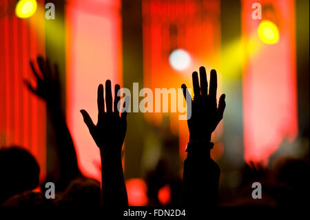 Audience soulève des mains en l'air lors d'un concert avec l'arrière-plan de couleur vive sur une scène. Projecteurs colorés brillants. Banque D'Images