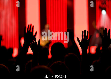 Audience soulève des mains en l'air lors d'un concert avec l'arrière-plan de couleur vive sur une scène. Projecteurs colorés brillants. Banque D'Images