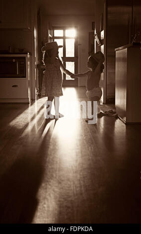 Image de deux soeurs se tenant la main et se regardant comme le soleil de l'après-midi dans les poutres entre elles. Banque D'Images