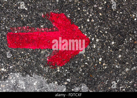 Une flèche rouge pointant vers la droite, peint avec de la peinture rouge sur l'asphalte. Banque D'Images