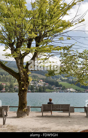 D'âge moyen aux cheveux rouge portrait femme assise sur un banc sous un grand arbre sur la rive du lac de Mondsee, Autriche Banque D'Images