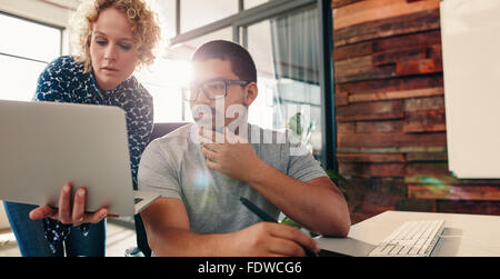 Portrait de jeune équipe de graphistes qui travaillent ensemble dans un nouveau projet, avec femme montrant quelque chose d'important d'une colle Banque D'Images