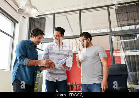 Équipe de jeunes gens créatifs discussing paperwork dans le bureau. Trois jeunes hommes Réunion de bureau moderne en passant par certains ne Banque D'Images