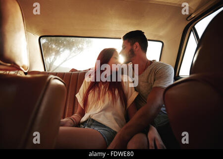 Young couple sitting in siège arrière d'une voiture. Jeune homme et de la femme de banquette arrière d'un véhicule avec sun flare. Banque D'Images