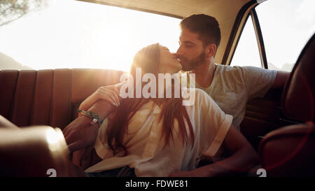 Couple assis en arrière d'une voiture et s'embrasser . Friends sur siège arrière d'un véhicule avec sun flare. Banque D'Images