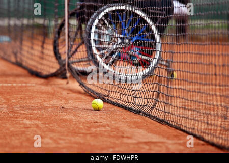 Joueur de tennis en fauteuil roulant non vu derrière un filet de tennis sur une cour d'argile Banque D'Images