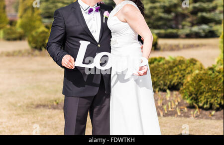 Bride and Groom holding bouquet et du mot amour en bois Banque D'Images