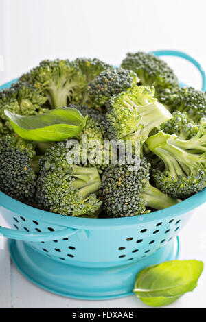 Bouquets de brocoli frais dans une passoire bleu sur blanc Banque D'Images