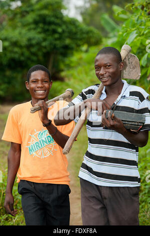 Deux jeunes hommes avec des houes sur leurs épaules retour à la maison après une journée de travail dans les champs. L'Ouganda. Banque D'Images