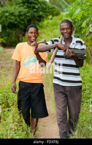 Deux jeunes hommes avec des houes sur leurs épaules retour à la maison après une journée de travail dans les champs. L'Ouganda. Banque D'Images