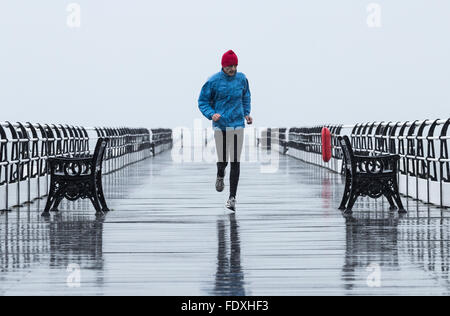 Mature man jogging sur Saltburn pier sous la pluie. Marseille par la mer. Yorkshire du Nord. UK Banque D'Images