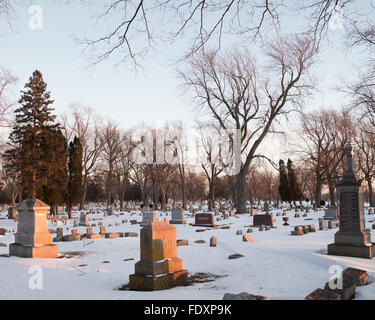 Lumière chaude les captures les pierres tombales et les pierres tombales d'un cimetière d'arbres et de la neige en hiver. Banque D'Images