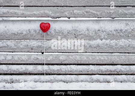 Sucette en forme de coeur rouge sur le banc de neige dans winter park Banque D'Images