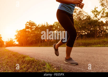 Femme de l'activité en cours d'exécution on rural road pendant le coucher du soleil Banque D'Images