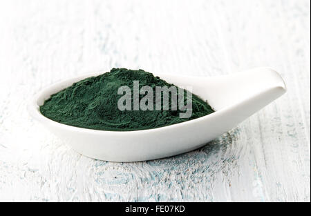 La spiruline en poudre cuillère en porcelaine blanche sur table en bois blanc Banque D'Images