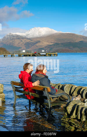 Le Loch Lomond, au Royaume-Uni. 3 Février, 2016. Après les récentes tempêtes et fortes pluies pour la saison, le niveau d'eau à Luss sur le Loch Lomond a surmonté les murs provoquant des inondations locales.Sur la première journée ensoleillée, Tom Wilson et la Géorgie à partir de Londres, en vacances près de Luss, prendre une promenade relaxante pour admirer la neige surmonté Ben Lomond et les eaux calmes du Loch Lomond. Credit : Findlay/Alamy Live News Banque D'Images