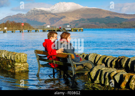 Le Loch Lomond, au Royaume-Uni. 3 Février, 2016. Après les récentes tempêtes et fortes pluies pour la saison, le niveau d'eau à Luss sur le Loch Lomond a surmonté les murs provoquant des inondations locales.Sur la première journée ensoleillée, Tom Wilson et la Géorgie à partir de Londres, en vacances près de Luss, prendre une promenade relaxante pour admirer la neige surmonté Ben Lomond et les eaux calmes du Loch Lomond. Credit : Findlay/Alamy Live News Banque D'Images