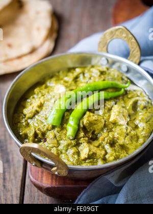 La cuisine indienne : Panir aux épinards dans un bol en cuivre traditionnel servi avec roti tandoori sur une table en bois sombre. Banque D'Images