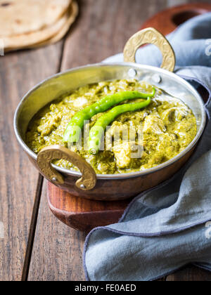 La cuisine indienne : Panir aux épinards dans un bol en cuivre traditionnel servi avec roti tandoori sur une table en bois sombre. Banque D'Images