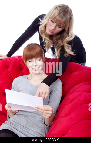 Jeune et belle blonde aux cheveux rouge filles sur canapé rouge afficher la lettre in front of white background Banque D'Images